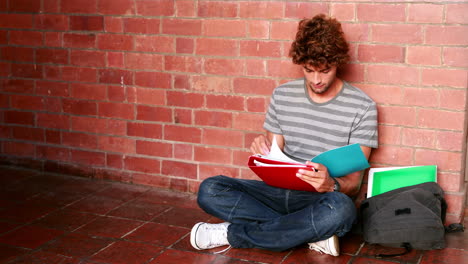 estudiante sentado contra la pared leyendo un libro de texto