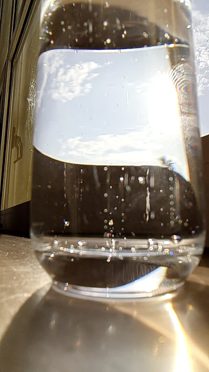 primi piani estremi al rallentatore di bolle in un bicchiere su una finestra alla luce del giorno e vista attraverso il vetro con impronta digitale