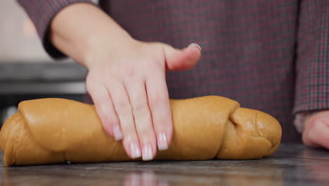 vista parcial de una mujer con una pulsera en la mano izquierda descansando en el mostrador de la cocina, amasando masa fresca con la mano derecha, preparando productos horneados caseros en una cocina moderna con una atmósfera acogedora