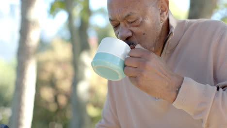 Happy-senior-biracial-man-using-smartphone-and-drinking-coffee-at-balcony-at-home,-slow-motion