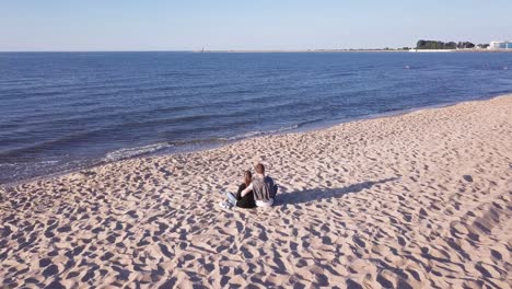 Aerial-Shot-Of-Young-Couple-Sitting-On-Sandy-Beach,-Hugging,-Holding-Hands