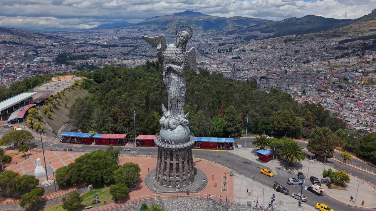 Il drone inizia con una ripresa ravvicinata dal basso verso l'alto della Vergine di Quito, poi si allontana per rivelare l'intera statua, il punto panoramico, la città tentacolare sottostante e le montagne circostanti sotto un cielo nuvoloso