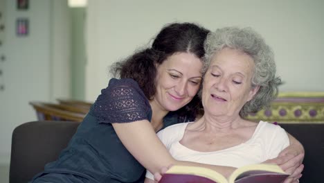 mother reading book aloud in living room, daughter hugging her