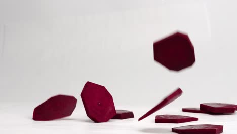 geometric beet slices falling and bouncing in slow motion on a white backdrop in 4k