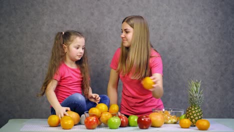 happy little girl and her mother with fruits at home. mother and daughter in pink t-shirts are having fun with fresh organic fruit in the kitchen.