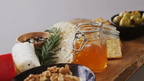 Bowl-of-green-olives,-bread,-jam,-rosemary-herb,-cheese-and-walnuts-on-wooden-board