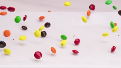 colorful m and m candies falling onto white plate and dancing around in slow motion