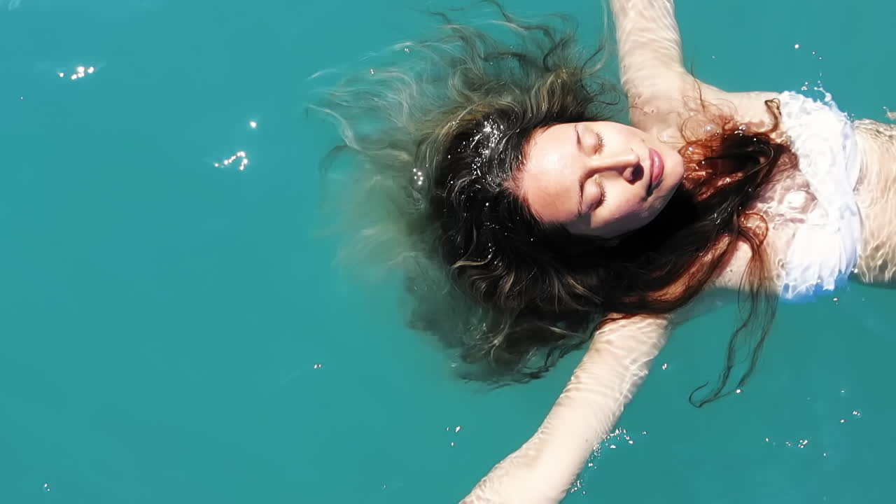 Caucasian woman in white swimsuit lying on green and transparent water. View from the top. Slow motion