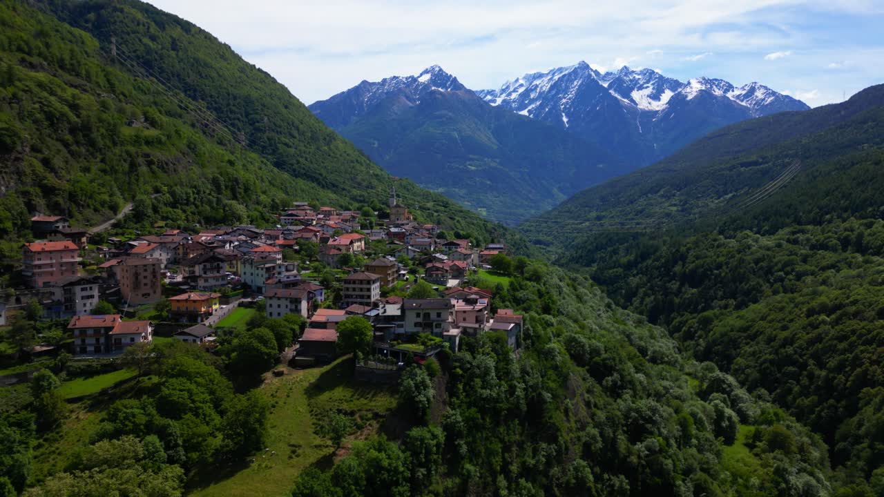 Tomada de drone de Malonno mostrando telhados vermelhos, terreno íngreme, floresta exuberante e os Alpes cobertos de neve ao fundo. Filmado em Malonno, Itália