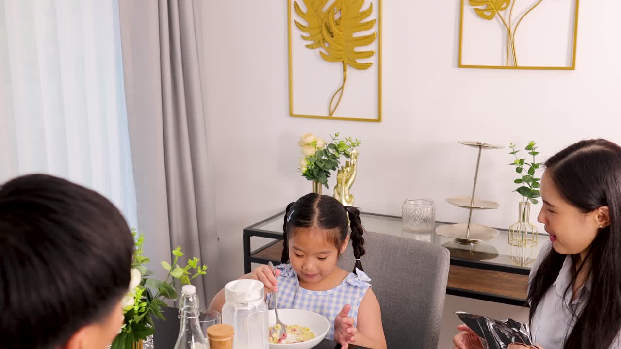 A family enjoys breakfast together, featuring a child eating cereal. Bright lighting and a cozy atmosphere enhance the scene