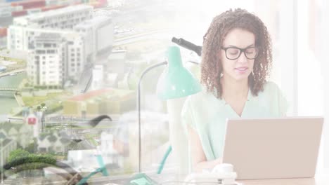 Animation-of-biracial-businesswoman-using-laptop-over-cityscape