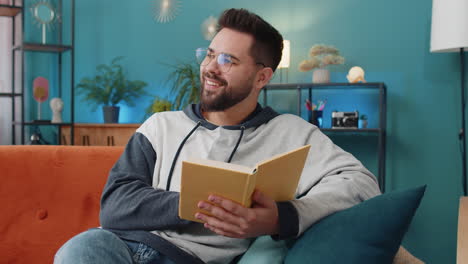 joven relajándose libro interesante volviendo páginas sonriendo disfrutando de la literatura descansando en el sofá