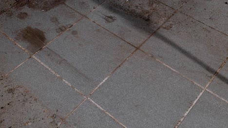 sweeping up dirt in a dust pan from a dirty tiled garage floor. static 4k shot.