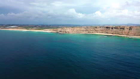 aerial-view-of-rugged-coast-line-with-blue-ocean-and-waves-crashing,-portugal,-4k