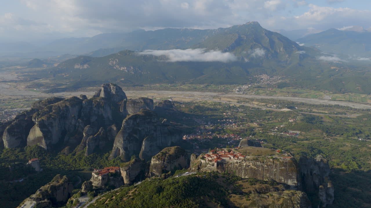 Cinematic aerial view of Meteora monastery in Greece perched on towering cliffs, dramatic rock formations and lush green valley create a breathtaking historic scene