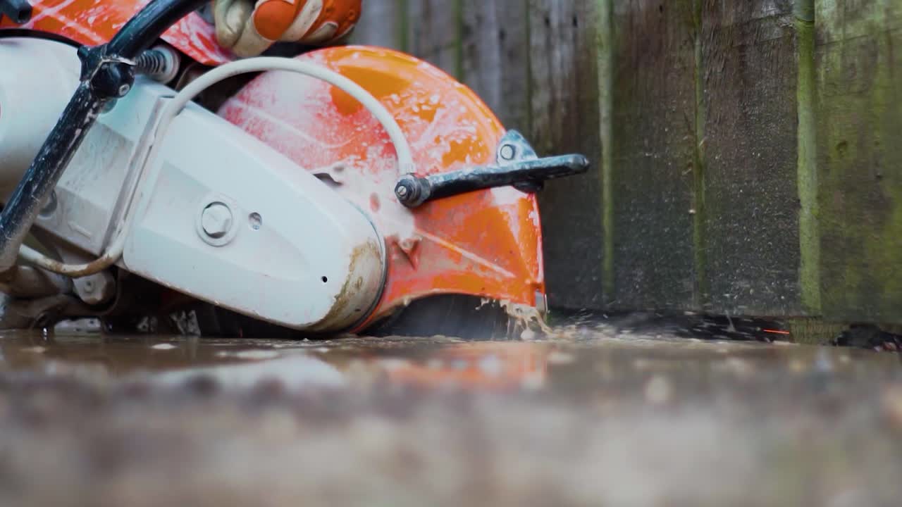 Petrol stone saw cutting through concrete with water dust suppression and safety gloves