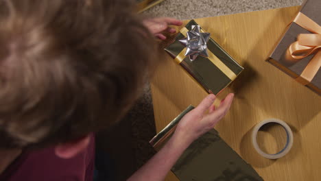 overhead shot of man wrapping and putting bow on gift or present on table at home