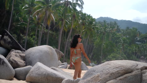 beautiful brunette woman in a bikini walking along a tropical rocky beach - slow motion