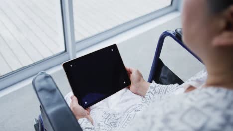 vista sobre el hombro de una paciente asiática sentada en silla de ruedas usando un teléfono inteligente en el hospital