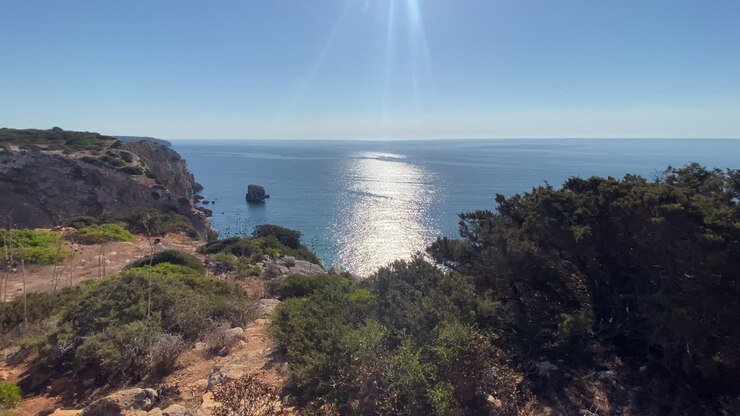 Arbustos verdes e falésias acidentadas emolduram as águas tranquilas do Atlântico ao longo da costa de Sagres.
