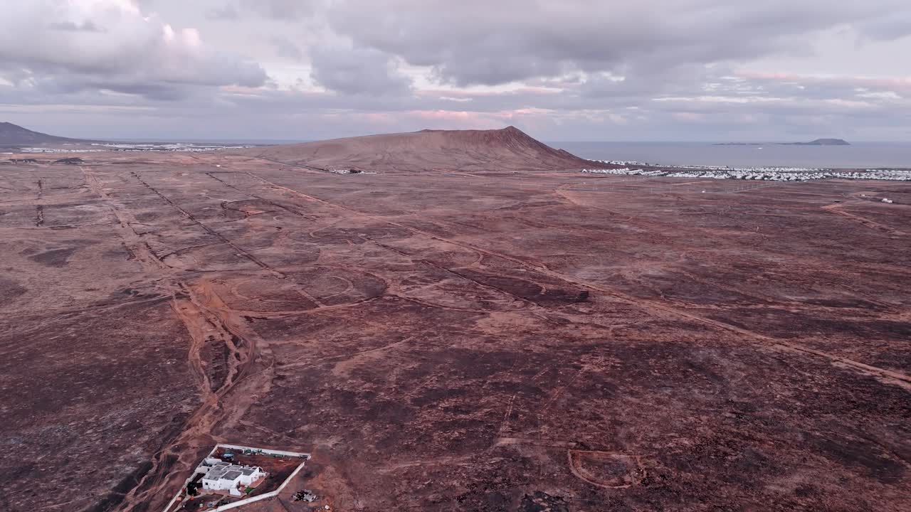 A stunning aerial drone shot capturing a solitary man walking along the rim of Volcano del Cuervo at sunset in Lanzarote, Canary Islands, Spain.