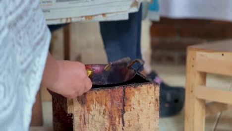 the "canting" tool for drawing batik is in a small frying pan on the stove and emits smoke and is then taken by a woman's hand