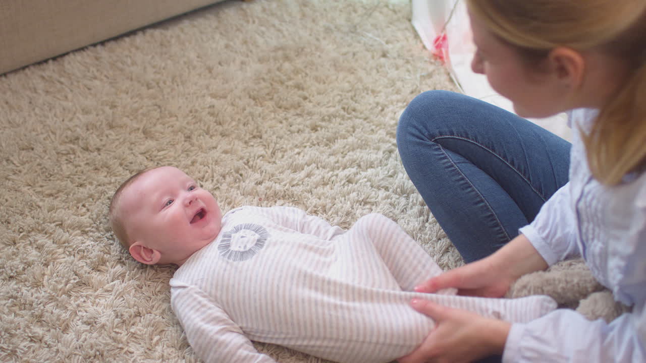 Loving mother playing game and tickling baby son lying on rug in child's bedroom at home - shot in slow motion