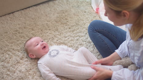 Liebevolle-Mutter-Spielt-Und-Kitzelt-Ihren-Kleinen-Sohn,-Der-Zu-Hause-Auf-Dem-Teppich-Im-Kinderzimmer-Liegt-–-Aufgenommen-In-Zeitlupe