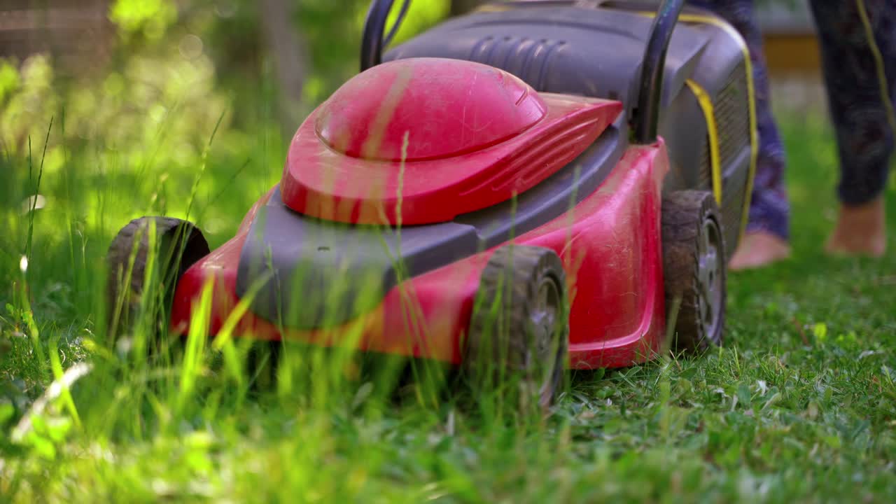 Lawn mower in the garden. Gardener mowing green grass in backyard. Electric mower machine in summer. Close-up.