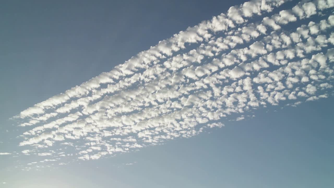 澄み切った青空を横断しながら、細長いさざ波状の雲の帯が密になりつつ漂い、太陽のまぶしさが差し込む