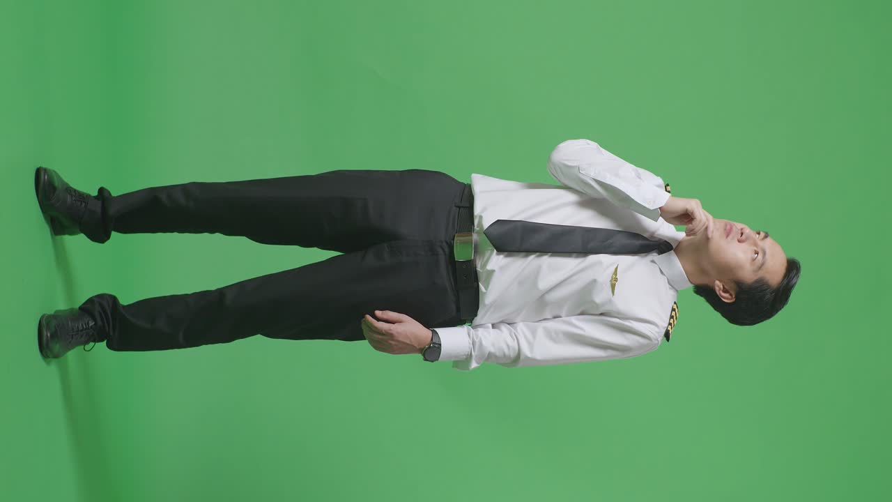 아시아 남성 조종사가 생각하고 주위를 둘러보며 초록색 스크린 배경 스튜디오에 서 있는 동안 지표손가락을 들어 올렸다.