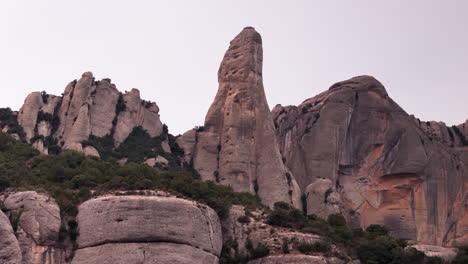 Drone-crane-down-shot-gracefully-revealing-the-round-cliff-peaks-of-Montserrat-against-the-backdrop-of-a-tranquil-overcast-day