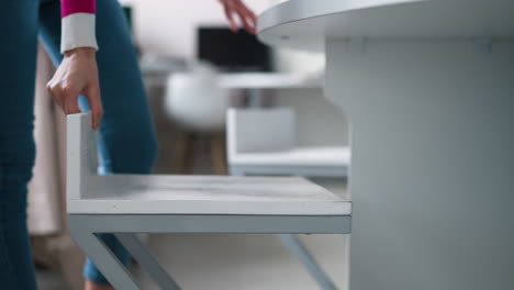 woman sits down on chair at table closeup. slim lady in jeans uses minimal wooden seat to rest at round desk. simple furniture for home interior