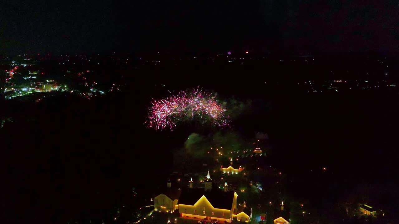 Colorful fireworks light up the night sky, creating a spectacular display above a vibrant town. People gather to enjoy the festivities while the sky bursts with color and energy