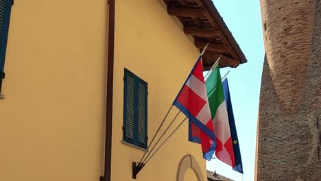 close-up of italian and eu flags on a sunlit building facade with blue shutters.