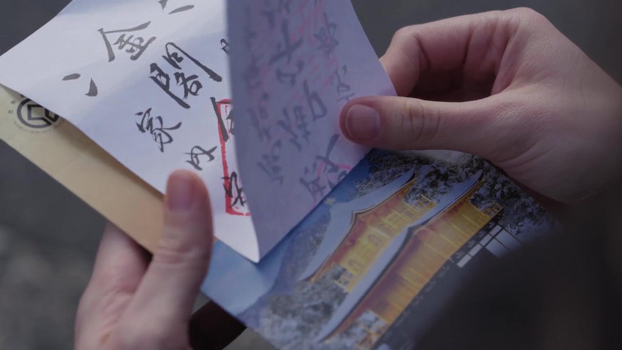 Mani che sfogliano le pagine di un libro di timbri di templi goshuin con calligrafia e stampa del Kinkakuji a Kyoto