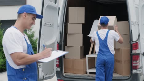 two young workers of removal company are loading boxes and furniture into a minibus