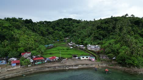 aerial rotating view of idyllic, coastal tropical village with lush rainforest-covered hill in background