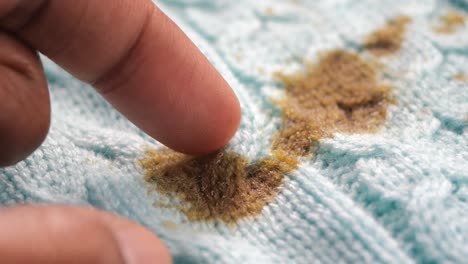 finger pointing at a brown stain on a light blue knitted fabric