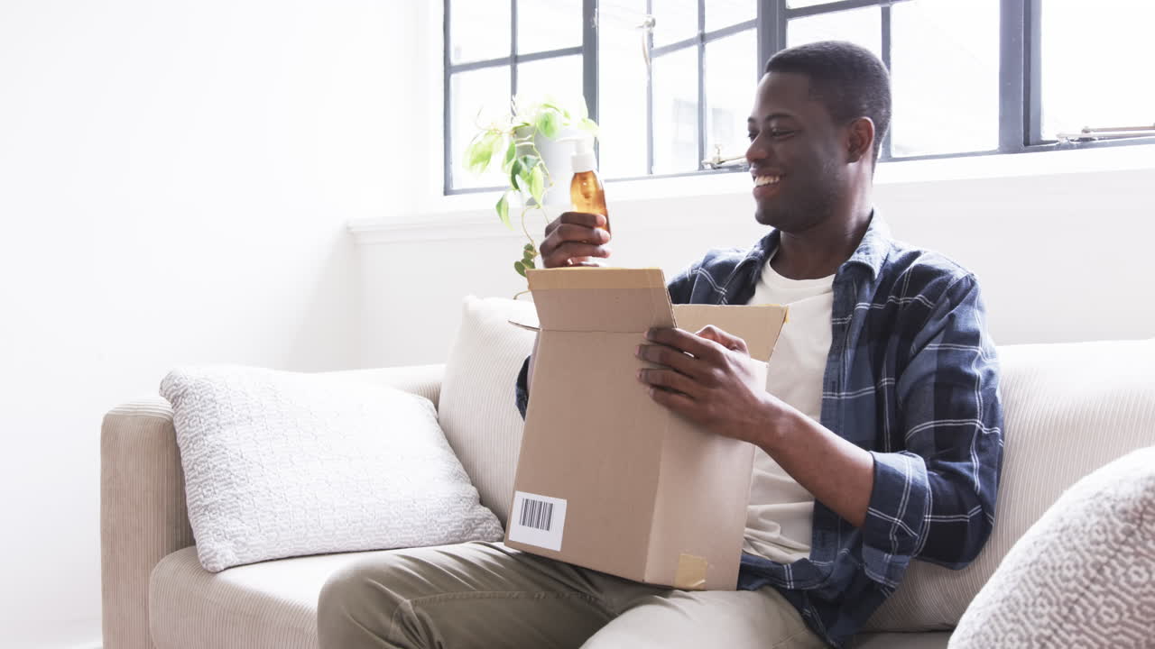 Smiling man opening gift box on couch, enjoying holiday surprise at home