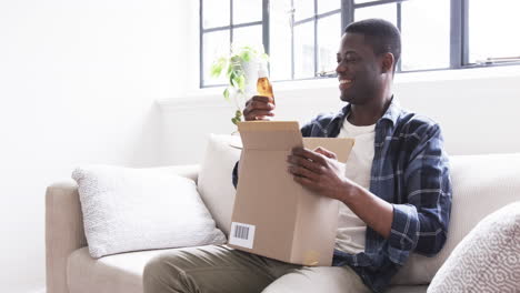 smiling man opening gift box on couch, enjoying holiday surprise at home
