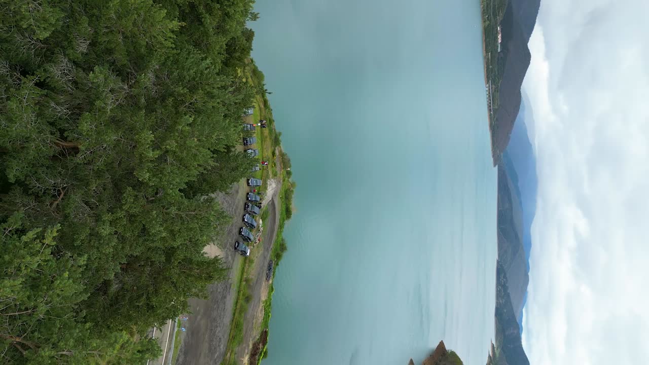 fotografía aérea vertical del lago riaño en picos de europa, españa, con cielos nublados, aguas azules tranquilas, acantilados de montaña y árboles verdes exuberantes