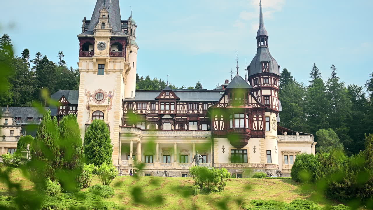 Utsikt over Peles-slottet i Romania. Slott med hager og turister i Karpatene, frodig skog rundt.