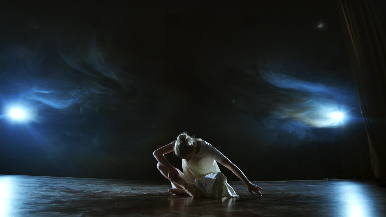 Slow motion: Modern ballet dancing woman barefoot lying on the floor doing spins and pirouettes and somersaults.