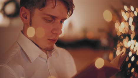 man reading novel in illuminated home during christmas