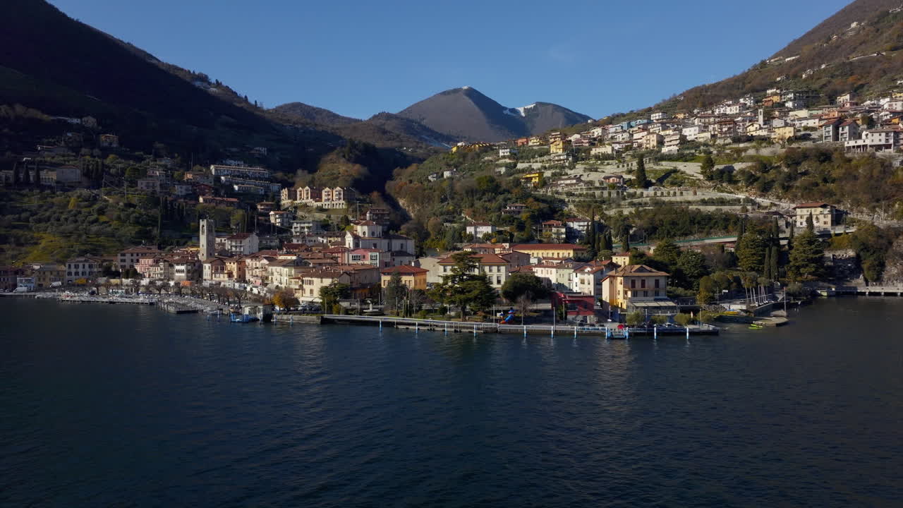Aerial view of scenic Italian lakeside town and comune, Tavernola Bergamasca, facing the calm turquoise waters of Lake Iseo