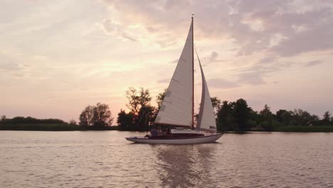 Side-panning-shot-of-sail-boat-cruising-on-calm-lake-at-Netherlands,-aerial