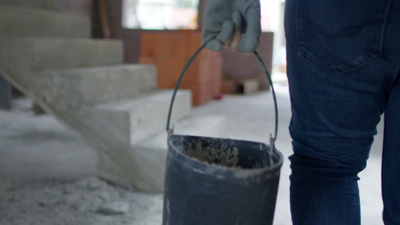 un primer plano extremo en cámara lenta de 4k de la mano de un trabajador agarrando el mango de un cubo, destacando el esfuerzo y el detalle en un sitio de construcción.