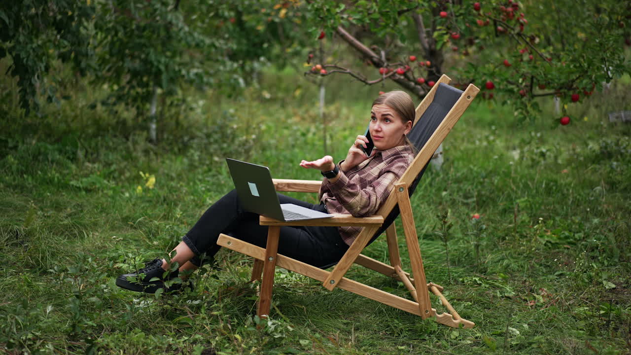 Busy lady working freelance speaks emotionally on the phone. Lady is puzzled about conversation. Opened laptop in front of woman.