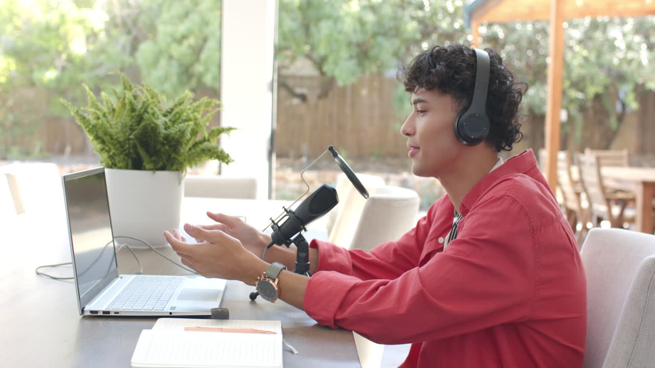Recording podcast, teenage boy with headphones speaking into microphone at home office